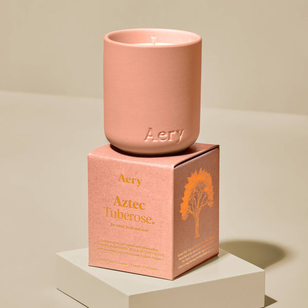 Pink candle with 'Aery' branding on a matching box against a beige background