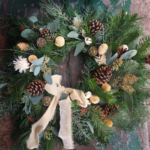 Christmas wreath with greenery, pinecones, and ribbons on a textured surface