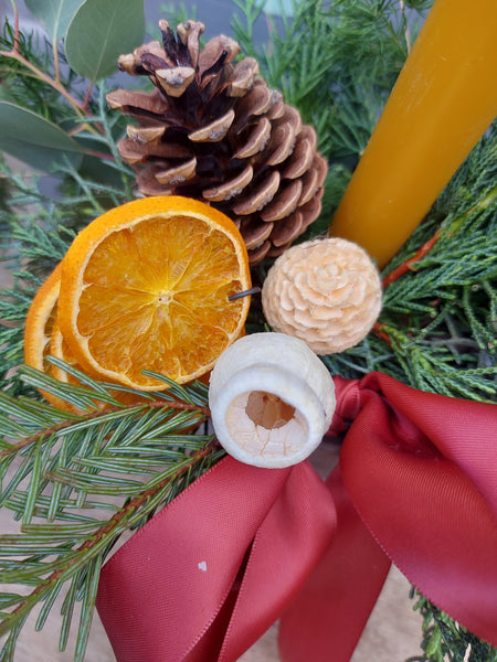 Decorative arrangement with pine cones, dried oranges, and a red ribbon.