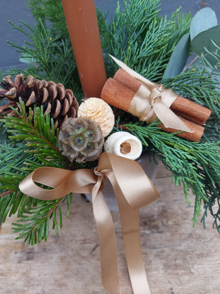 Decorative arrangement with candles, pine cones, and ribbons on a wooden surface